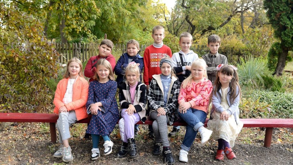 Happy group of kids sitting on a bench in a park during fall, enjoying a sunny day.
