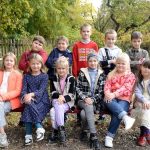 Happy group of kids sitting on a bench in a park during fall, enjoying a sunny day.