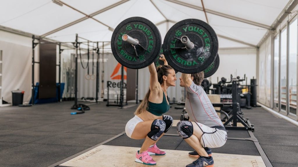 A couple lifting weights together in a gym, promoting fitness and teamwork.
